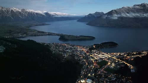 Resort destination Queenstown on lakeshore, surrounded by mountains. Night lights, drone shot. New Z
