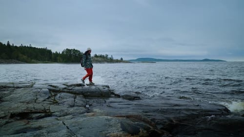 Walk In Nature In Autumn Day Woman In Active Wear With Backpack Strolling On Stone Shore Of Lake