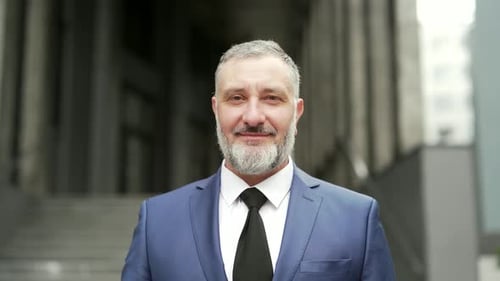 Porträt glücklicher reifer grauhaariger bärtiger Geschäftsmann. Geschäft im urbanen Hintergrund in die Kamera schauen