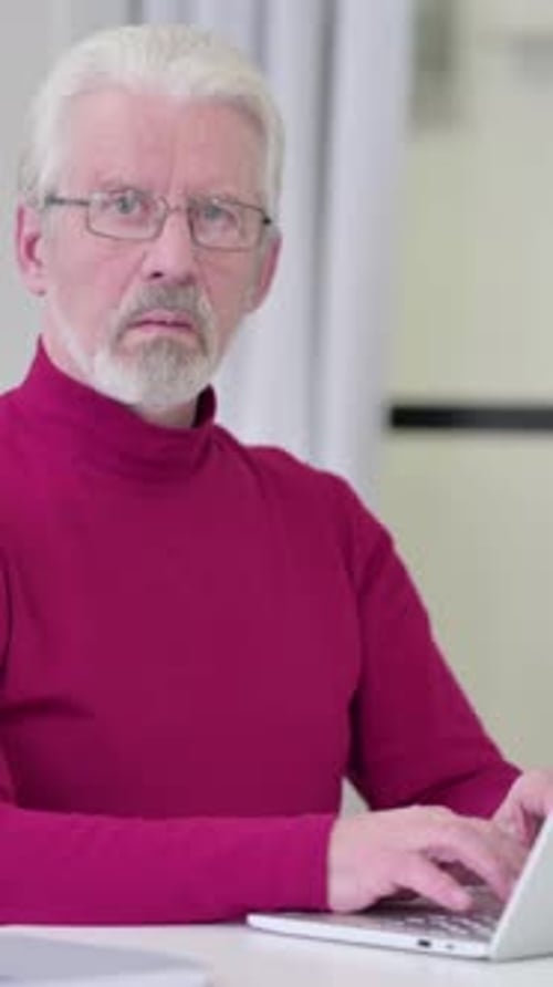 Senior Man with Gray Hair Works on Laptop