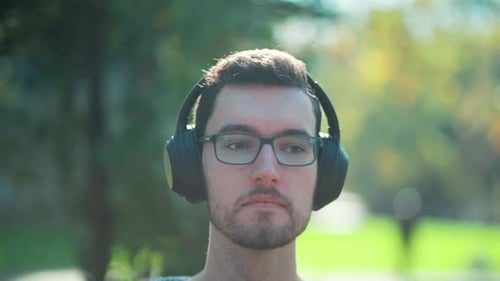 man dude glasses wears headphones sitting in park listens to music to vibe relax. Closeup portrait y