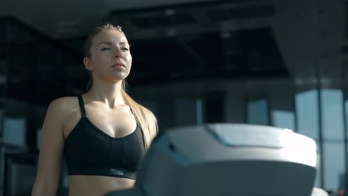 Portrait of Young Woman Walking on Treadmill Looking Away in Gym