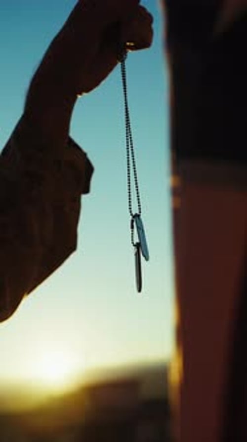 Man Holding Dog Tags at Sunrise