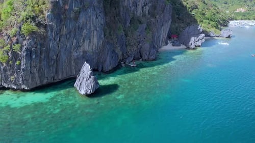 Retreating flight along dramatic karst limestone cliffs dropping into crystal clear turquoise