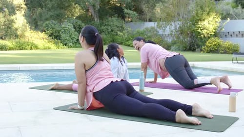 Diversas mujeres haciendo yoga junto a la piscina sobre colchonetas con botellas, mujer levantándose y atrayendo a una joven