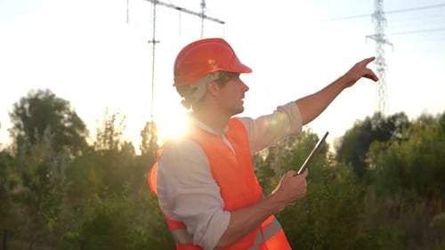 Engineer with Tablet Inspecting Powerlines at Sunset