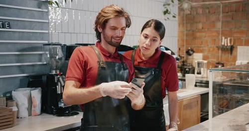 Baristas Looking At Phone Together Inside Coffee Shop