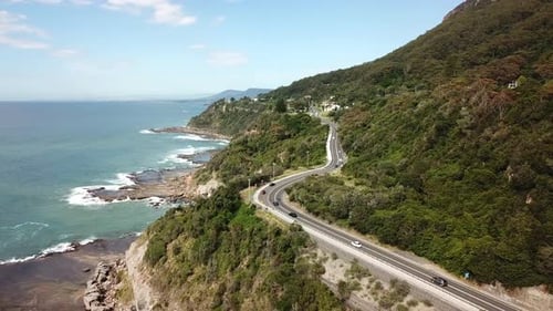 Aerial: Drone flying over vehicles driving along a highway next to a beautiful ocean coastline, in