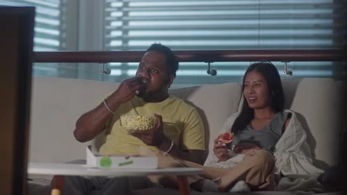 Couple Laughing, Watching TV and Eating Junk Food