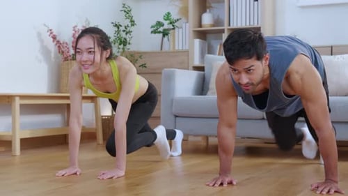 Happy young asian couple workout with doing mountain climbers exercise together in living room.