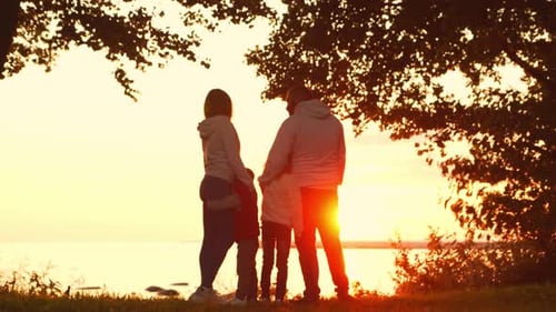 Family Silhouette Watching the Sunset Over Water