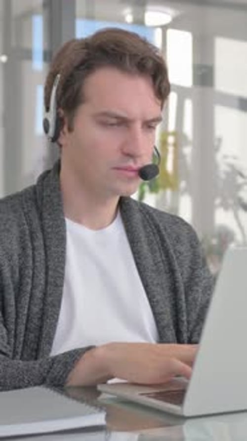 Young Man with Headset in Call Center Working on Laptop, vertical video