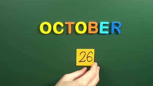 Hand sticking a sticker 26 October calendar day on school board. 26 date of October. Twenty sixth