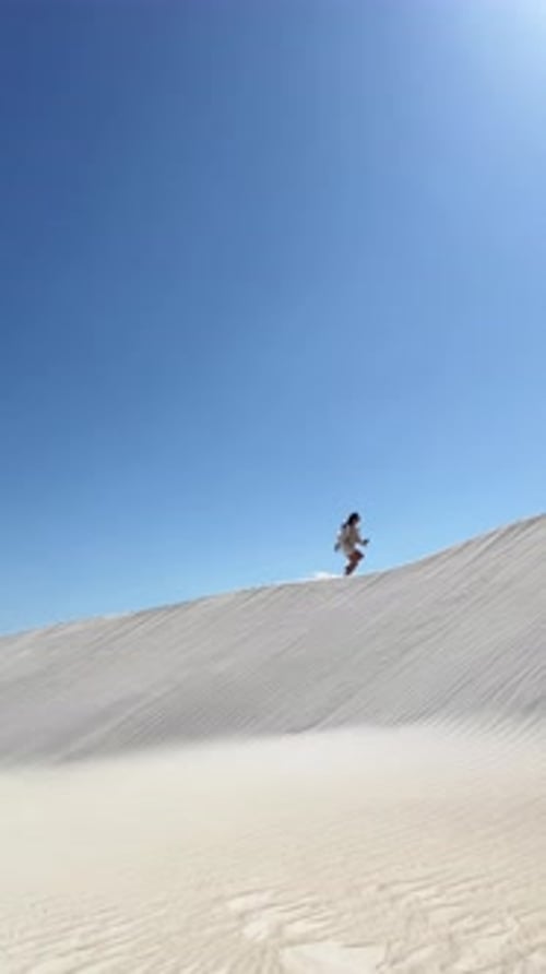 Woman climbs a sandy dune under the clear blue sky in a desert landscape during a bright sunny day