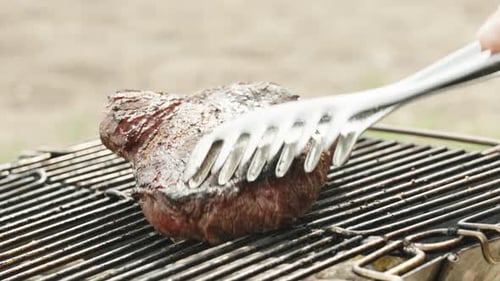 Using tongs, I flip the steak on the grill, ensuring it gets a delicious sear on both sides.