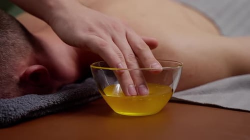 Massage mit Honig Die Hand eines Mannes nimmt gelben Honig aus einer durchsichtigen Tasse, um einen Neugierigen zu massieren