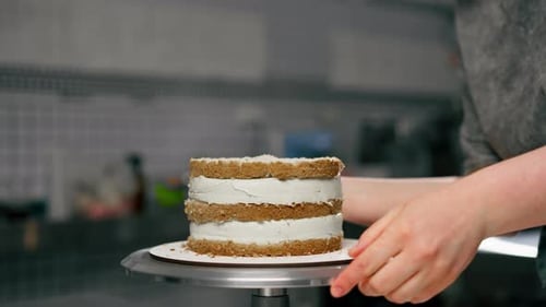 Nahaufnahme Eine Bäckerin in einer professionellen Küche gibt Sahne aus einem Spritzbeutel auf einen Biskuitkuchen