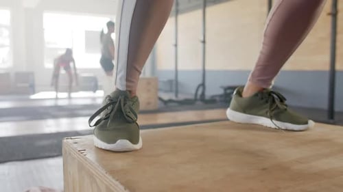 Low section of unaltered woman jumping on box, training at fitness class in gym, slow motion