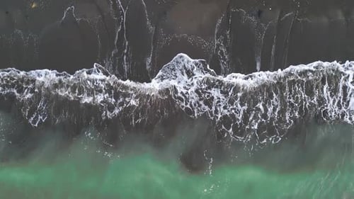 Aerial view of sea waves crashing on black sand beach