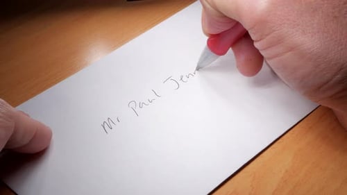 Man writes an address on a white envelope.
