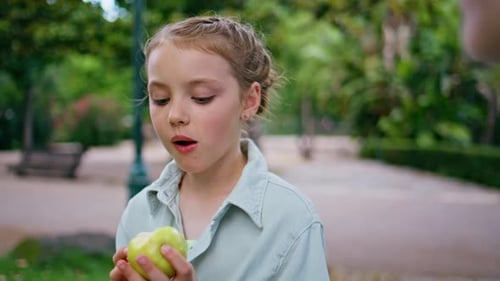 Kleines Mädchen isst Apfel im Park Portrait Kleines Kind genießt leckeres Obst