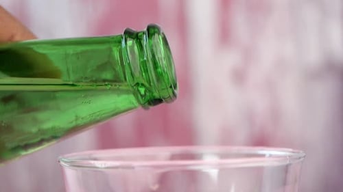 Pouring Clear Liquid from Green Bottle into Glass
