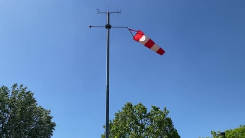 Red and white windsock blowing in the wind against a clear blue sky.
