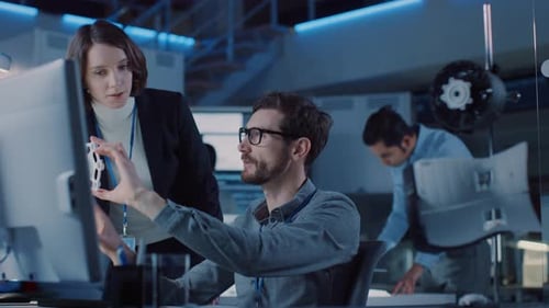 Futuristischer Entwicklungsingenieur für Maschinenmotoren arbeitet an seinem Schreibtisch am Computer und spricht mit weiblicher P