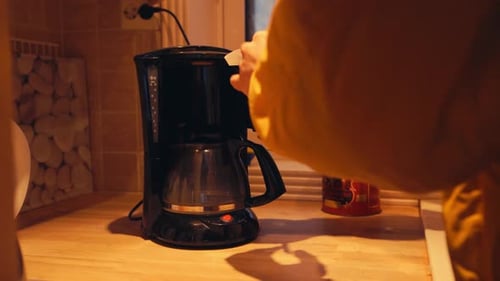 Une personne ouvre le compartiment d'égouttage d'une cafetière et y met du marc de café. Faire du café avec le kit