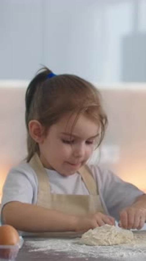 Little Girl in Kitchen Apron Kneading Dough with Floury Hands on Countertop Learning Homemade Baking