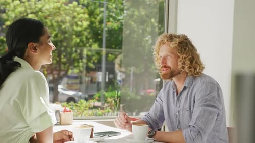 Happy diverse couple drinking coffee and talking at a table in cafe