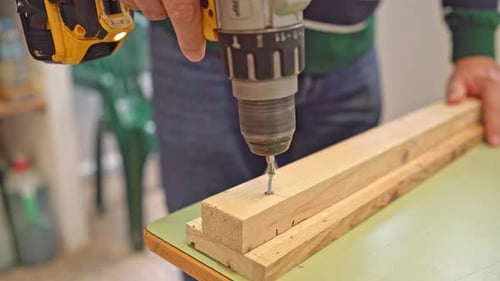 Close-up of a worker's hands using a cordless screwdriver to drive a screw into a piece of wood