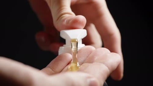 Nahaufnahme der Hände mit einem Pumpspender, bei dem Creme oder Lotion austreten, dunkler Hintergrund betont