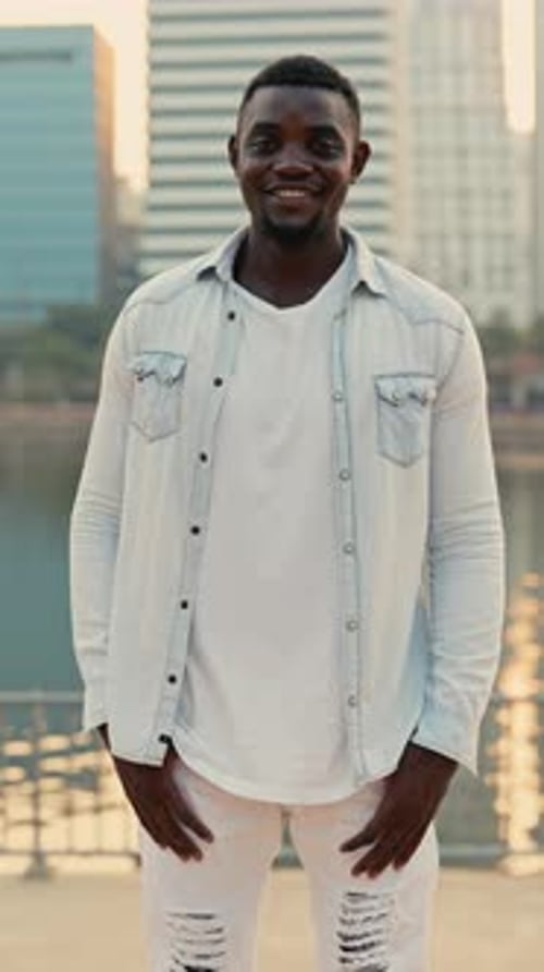 Positiver bärtiger Afroamerikaner steht auf dem Damm und schaut in die vertikale Aufnahme der Kamera