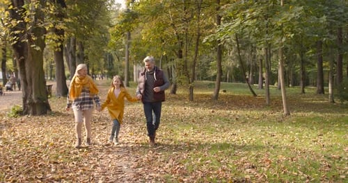Small Girl with Grandparents on a Walk in Autumn Forest