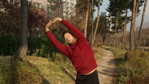 Mid Adult Man Active Exercising Outdoors in a Park Trail Stretching Torso Locking Arm Above Head and