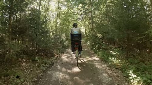 Mother and her child at the back seat of her bike are going to take a ride through a green sunny for
