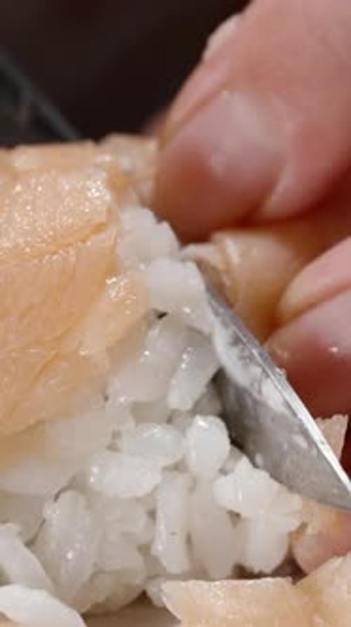 Vertical video. The woman cuts the sushi rolls with salmon and the filling of cream cheese