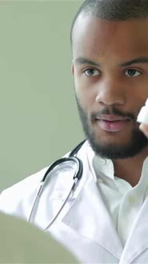 Male Doctor Holding Bottle of Pills in Clinic