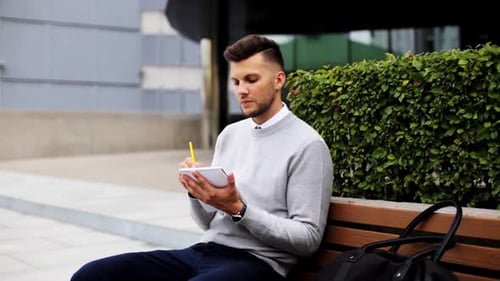 Man Writing in Notebook on Bench