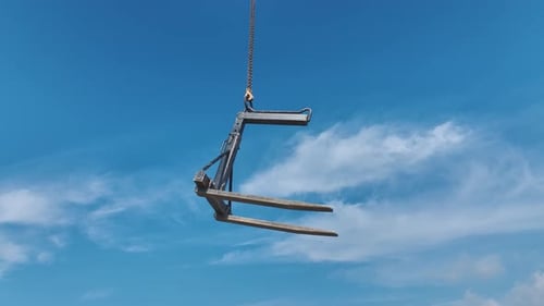 Forklift Attachment Suspended by Chain Against Blue Sky