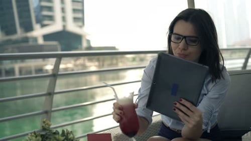 Young businesswoman enjoys beverage browsing tablet computer at cafe in the city