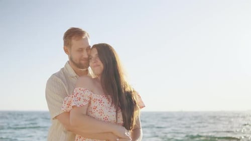 A Couple Embraces Tenderly at the Beach During Sunset with Gentle Waves Lapping Nearby and a Warm