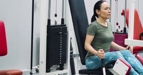 Uma mulher de meia idade treina os músculos das pernas com a máquina de abdução de pernas