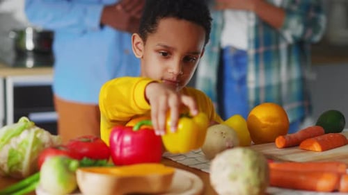 Child Plays with Vegetables at Table in Kitchen
