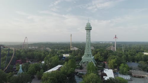 Drone soars over an empty theme park on a sunny morning. Roller coasters and towers line the skyline