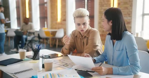 Women Do Paperwork Sitting at Table Against Men in Office