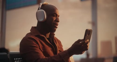 Male Professional Using Smartphone and Headphones for Video Meeting at Airport
