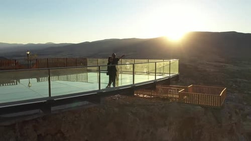 Aerial View Of Couple Watching The View From The Glass Terrace At Sunset