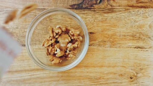 Pouring Walnuts into Glass Bowl on Wooden Surface